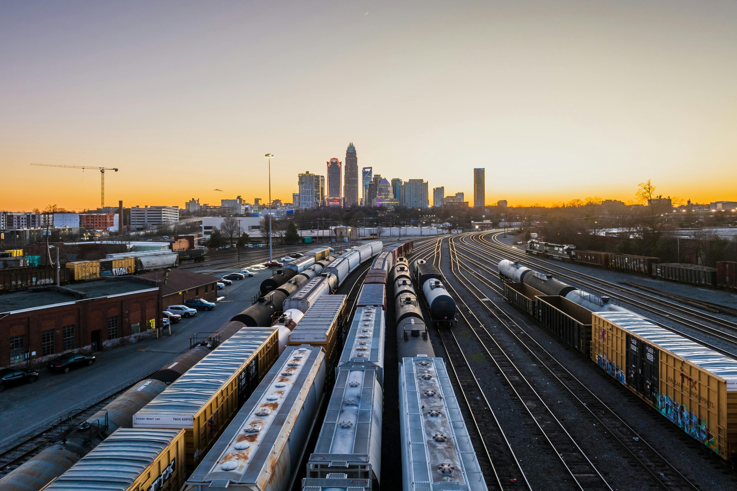 Dramatic sunset over Charlotte's skyline with cargo trains heading into the city, showcasing transportation and urban life.